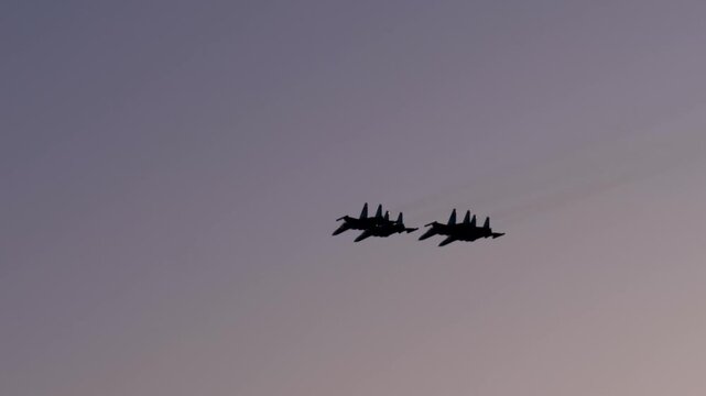 Four military fighter jets flying in a synchronized formation, silhouetted against the colorful sky during a beautiful sunset, performing maneuvers. Patriotic airshow demonstration