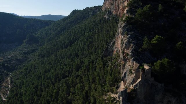 Mallorca landscape: sheer rock face and remnants of stone fortification above forested slopes