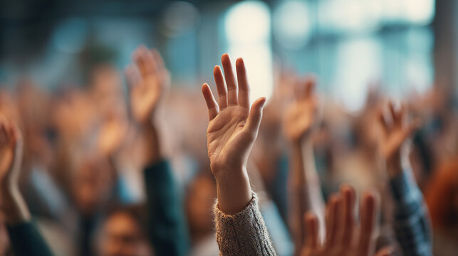 A diverse crowd of people raising their hands during a meeting, showing active participation, engagement, and teamwork in a bright, professional setting. - Powered by Adobe