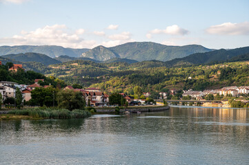 Fototapeta premium A small coastal town with houses and buildings, located by a calm river, surrounded by wooded hills