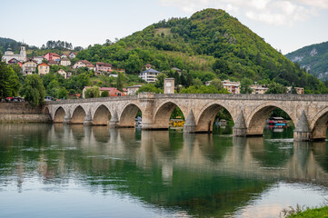 An ancient stone bridge with arches spanning the tranquil Drina River