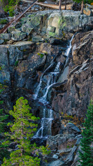 Scenic waterfall cascading down rugged granite cliffs surrounded by pine trees in Emerald Bay State Park at Lake Tahoe California USA, captured during summer in clear daylight from mountain trail