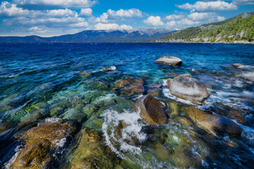 Lake Tahoe California USA view of clear turquoise water with granite rocks and pine forest along mountain shore under blue sky with clouds scenic summer landscape of Sierra Nevada nature