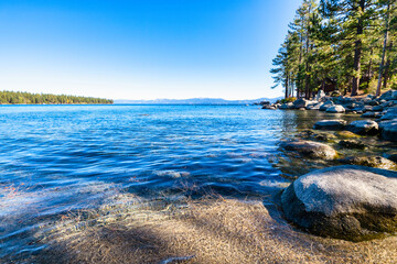 Lake Tahoe California USA clear blue lake with rocks on the shore and pine trees along the coast under sunny sky serene natural landscape and popular travel destination in the Sierra Nevada mountains