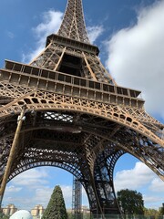 Fototapeta premium Dramatic low-angle photograph looking up through the iron structure of the Eiffel Tower against broken clouds