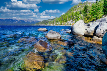 Lake Tahoe California USA view of clear turquoise water with granite rocks and pine forest along mountain shore under blue sky with clouds scenic summer landscape of Sierra Nevada nature