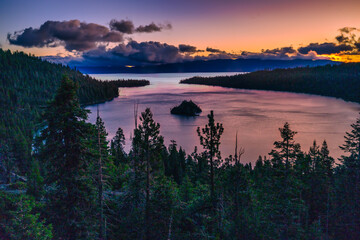 Emerald Bay State Park at Lake Tahoe California USA sunrise view with Fannette Island reflecting calm pink water surrounded by pine forest mountains and dramatic colorful sky scenic nature landscape