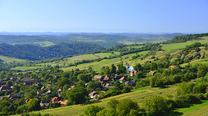 Late spring landscape in the hills of Transylvania. Village and church surrounded by lush greenery. 