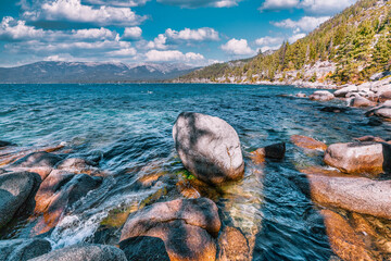 Lake Tahoe California USA view of clear turquoise water with granite rocks and pine forest along mountain shore under blue sky with clouds scenic summer landscape of Sierra Nevada nature