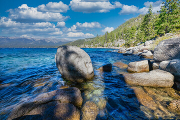 Lake Tahoe California USA view of clear turquoise water with granite rocks and pine forest along mountain shore under blue sky with clouds scenic summer landscape of Sierra Nevada nature