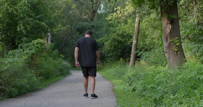 A man walks along path in green spring forest, limping on one leg