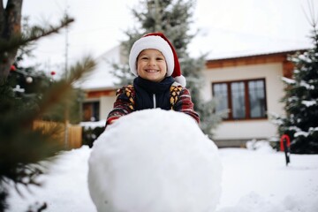 Child Wearing Santa Hat Building Snowman in Winter Garden