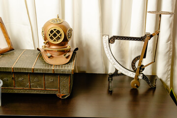 Vintage diving helmet and mechanical steelyard scale displayed against white curtain in Colombian interior.