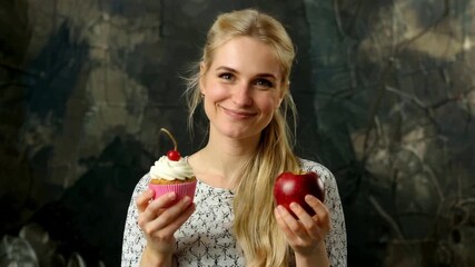 Smiling young woman choosing between a healthy red apple and a sweet cupcake with a cherry. Represents diet, temptation, and making a food choice - Powered by Adobe