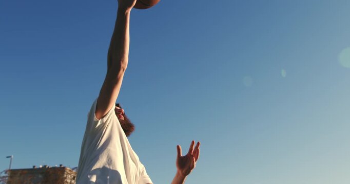 Slow motion close up of young athletic sportsman jumps to dunk a basketball on an outdoor court. Golden hour light, athletic energy, and street sport atmosphere.
