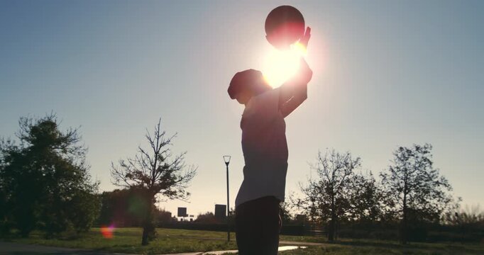 Slow motion of young athletic sportsman jumps to dunk a basketball on an outdoor court. Golden hour light, athletic energy, and street sport atmosphere.