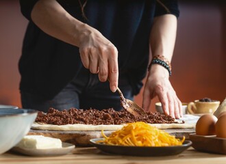Hands carefully spread sweet chocolate filling onto a long strip of dough. Butter, eggs, and orange zest sit nearby ready for the final touches on this delicious dessert