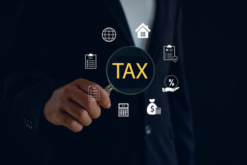 Businessman holding magnifying glass with TAX text and financial icons, representing tax audit, financial analysis, digital accounting, business management, and financial technology concept.