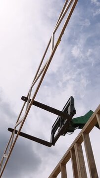 Workers use telehandler lift to position wooden truss in building under construction as clouds gather above.