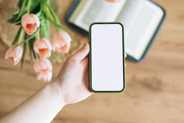 Phone in hand with isolated screen, on the home background with Bible.