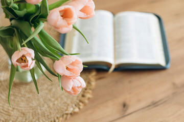 Open Bible and a bouquet of pink tulips on a wooden table at home. Copy space.