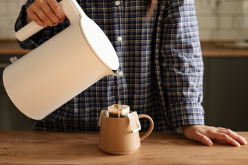 Woman pouring hot water into a cup with paper drip coffee bag at home.