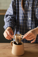 Woman hand holding cup with black coffee and drip filter on kitchen table.