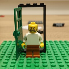 Naklejka premium Lego minifigure with an angry expression stands in an open doorway on a green baseplate, representing a concept of unwelcome entry or disagreement