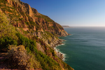 Breathtaking coastline view along Chapman&rsquo;s Peak Drive near Hout Bay, Cape Town, Western Cape; rugged cliffs, blue ocean, winding road, iconic South African landscape under clear sky.