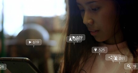 Asian woman wearing pink sweater scrolling tablet in cafe, with social metric overlays, copy space