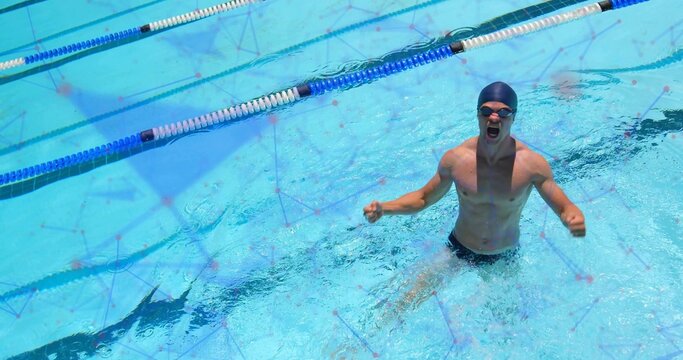 Emerging male swimmer raising fists from lane dividers in blue water, with swim cap goggles briefs