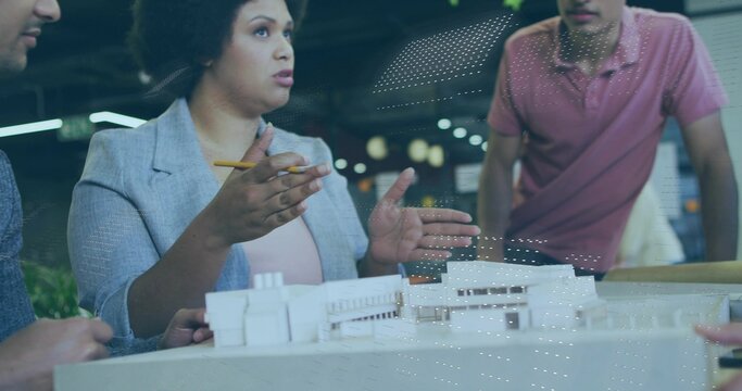 Presenting woman architect wearing blazer, gesturing with pencil at model in studio, with coworkers