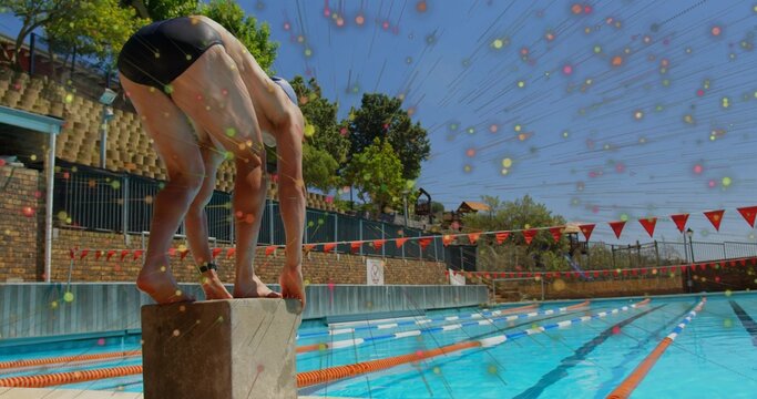 Crouching swimmer gripping starting block at lap pool, with lane ropes and flags, copy space