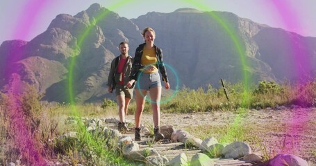 Walking couple wearing hiking boots traversing mountain trail, with logs stones shrubs lens flare