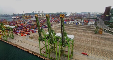 Showing three green gantry cranes lifting containers at busy seaport, with trucks and curved ramp