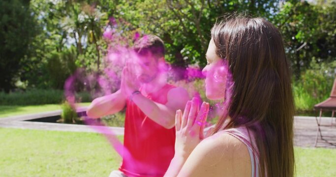 Sitting couple meditating in sportswear on grassy lawn near water feature, with pink powder cloud