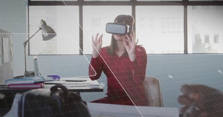 Reaching out worker wearing red dress VR headset at office, engaging VR interface with laptop