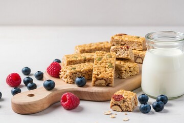 Oatmeal muesli bars on a wooden board, next to blueberries, raspberries, a jar of yogurt, bright shot, stock clear image
