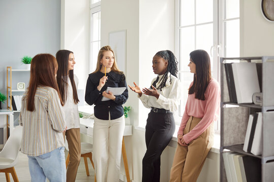 Diverse group of five women discussing in professional workplace environment, girls team unity and collaboration, start up positive emotions, friends together posing with confidence in modern office 