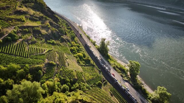 Aerial view of train and cars following river road below steep terraced vineyards. Regional train and river road along vineyards in the Upper Middle Rhine Valley, Rhineland Palatinate, Germany. 