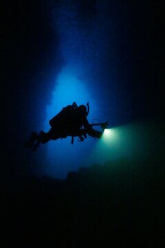 Scuba Diver Exploring Deep Waters in Gal&aacute;pagos &ndash; Silhouette with Flashlight in Submarine Cave or Trench