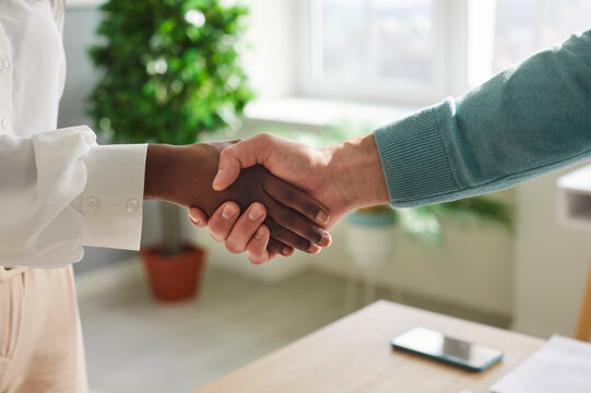 Cropped closeup photo of business african american woman standing in office on workplace shaking hands with a man colleague reaching agreement making a good deal or signing a contract.