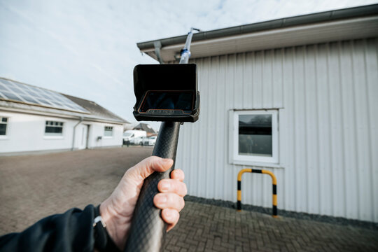 Technician using pole inspection camera to check rain gutter on residential building