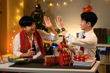 Two young office workers high-five in festive spirit during a joyful Christmas party with drinks,...