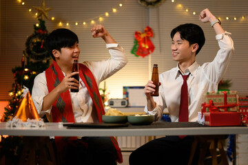 Office workers celebrate Christmas together, raising drinks and smiling in a cozy, decorated workspace