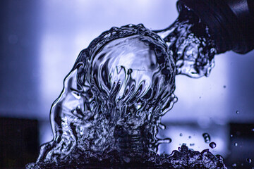 A dynamic macro shot of a light bulb being poured over by water, creating a unique abstract shape with smooth waves and cool blue-toned reflections.