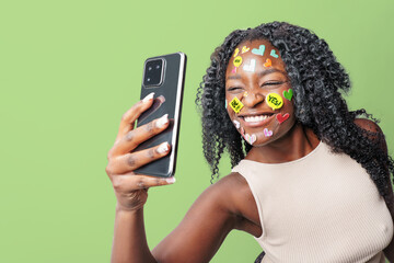  Portrait of carefree woman with make up with stickers on face, taking selfie against colorful background. social media addiction, communication concept.