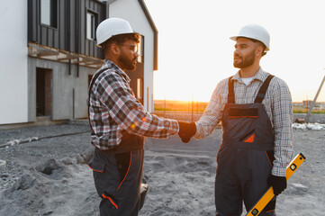 Construction workers handshaking on building site at sunset