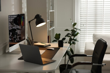 Stylish workplace with computer, laptop, cup, stationery and mat on desk, closeup