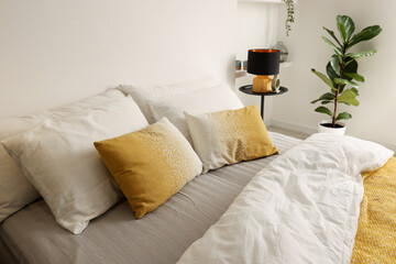 Large bed with linens, bedside table and houseplant near white wall in bedroom
